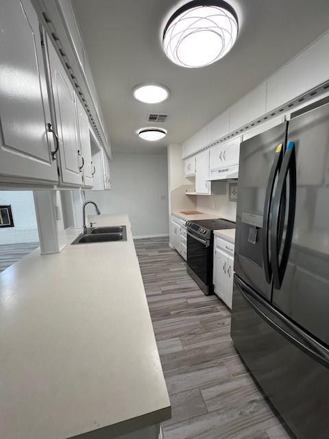 kitchen with visible vents, electric range oven, wood finished floors, black fridge, and a sink