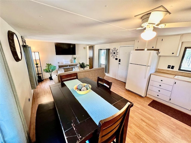 kitchen with light countertops, light wood-style flooring, a ceiling fan, freestanding refrigerator, and white cabinetry