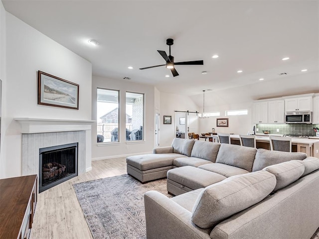 living area with ceiling fan, a tile fireplace, light wood-style flooring, recessed lighting, and baseboards