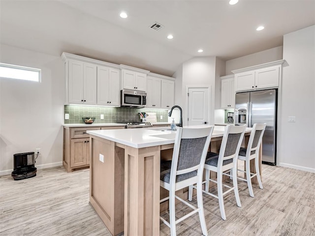 kitchen with a kitchen island with sink, light wood-style flooring, visible vents, appliances with stainless steel finishes, and backsplash