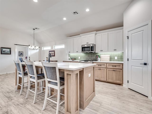 kitchen with stainless steel microwave, a center island with sink, visible vents, and backsplash