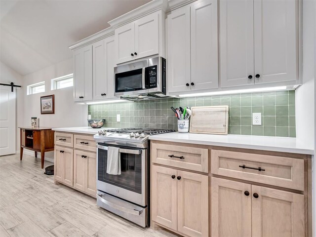 kitchen featuring stainless steel appliances, a barn door, light countertops, and decorative backsplash