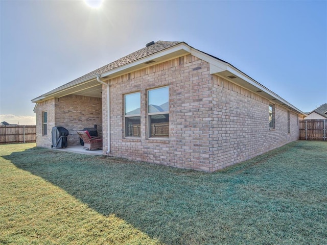 view of property exterior with a yard, brick siding, a patio, and a fenced backyard