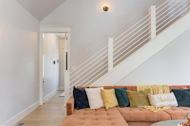 living room featuring lofted ceiling, light wood-style floors, stairs, and baseboards