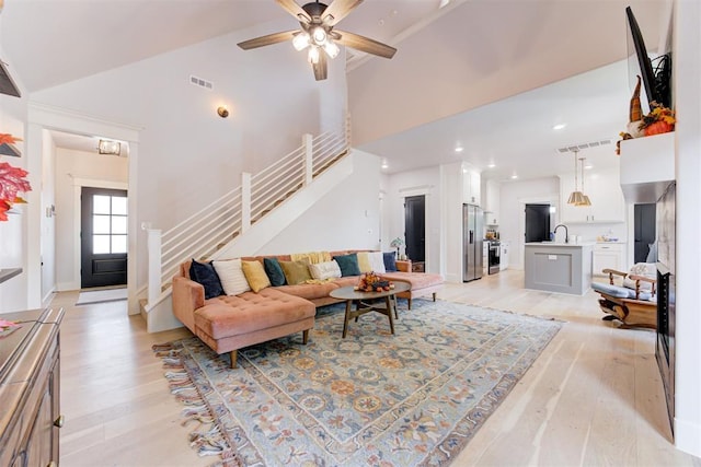 living room with light wood finished floors, stairs, visible vents, and high vaulted ceiling