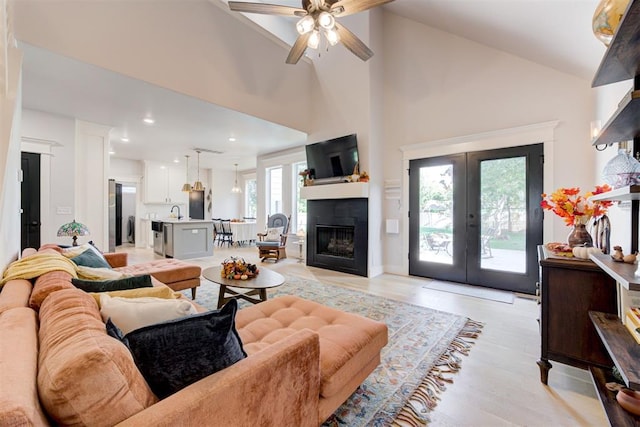 living room with a glass covered fireplace, ceiling fan, french doors, high vaulted ceiling, and recessed lighting