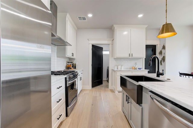 kitchen featuring stainless steel appliances, visible vents, white cabinetry, a sink, and wall chimney exhaust hood