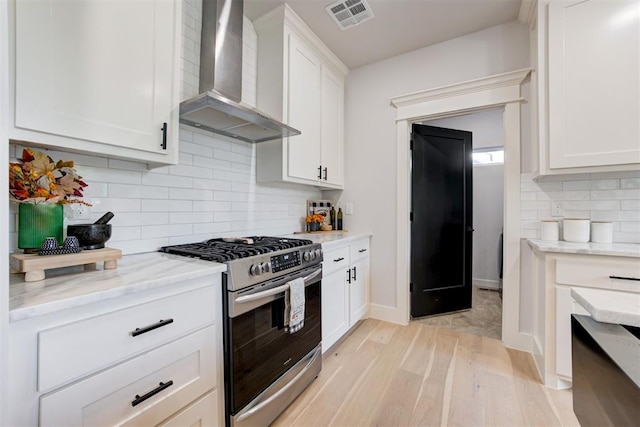 kitchen featuring visible vents, gas stove, white cabinetry, wall chimney range hood, and light wood-type flooring