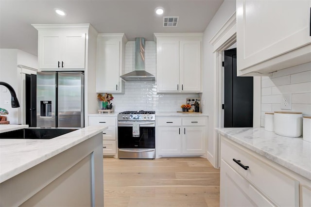 kitchen with light wood finished floors, recessed lighting, appliances with stainless steel finishes, white cabinets, and wall chimney exhaust hood