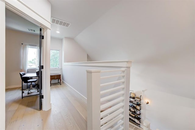 hall featuring vaulted ceiling, light wood finished floors, an upstairs landing, and visible vents