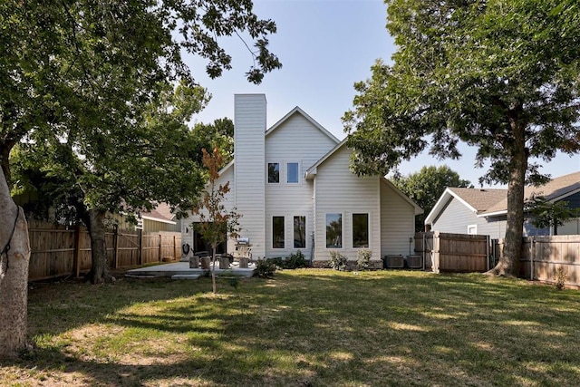 rear view of house with a fenced backyard, a chimney, cooling unit, a yard, and a patio area