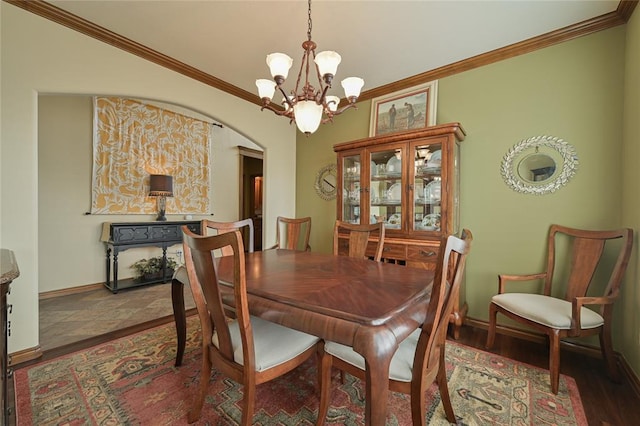 dining space featuring arched walkways, ornamental molding, wood finished floors, and baseboards