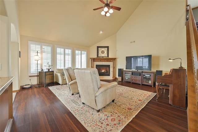 living area featuring high vaulted ceiling, dark wood-type flooring, a glass covered fireplace, and a ceiling fan