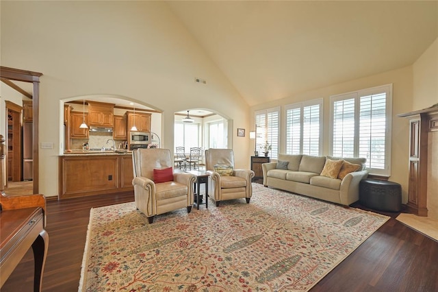 living area with high vaulted ceiling, visible vents, arched walkways, and dark wood-style flooring