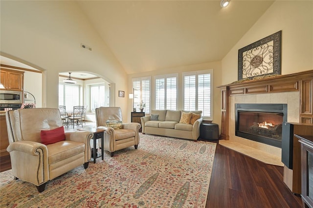 living area with visible vents, arched walkways, dark wood-style floors, a fireplace, and high vaulted ceiling