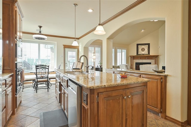 kitchen featuring stainless steel dishwasher, a sink, a kitchen island with sink, and brown cabinets