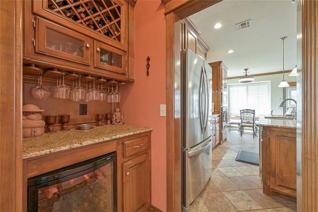 kitchen with beverage cooler, visible vents, freestanding refrigerator, and brown cabinets