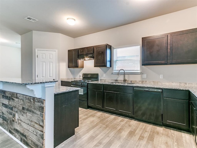 kitchen featuring a sink, light stone countertops, light wood-type flooring, under cabinet range hood, and black appliances