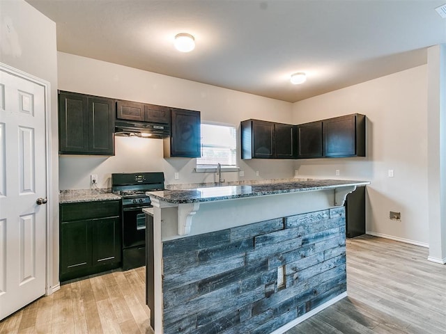 kitchen with under cabinet range hood, black range with gas cooktop, light wood-style flooring, and stone countertops