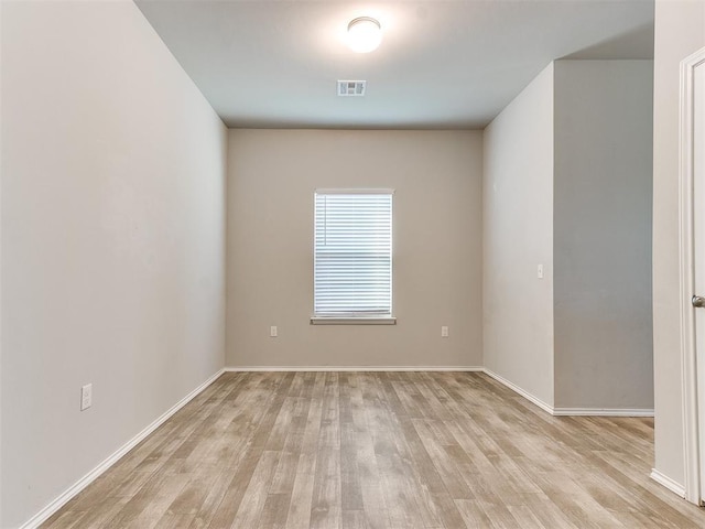 empty room with light wood-style floors, visible vents, and baseboards