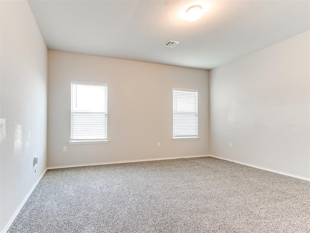 carpeted spare room featuring a wealth of natural light, visible vents, and baseboards