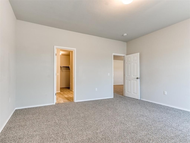 unfurnished bedroom with light colored carpet, a spacious closet, and baseboards