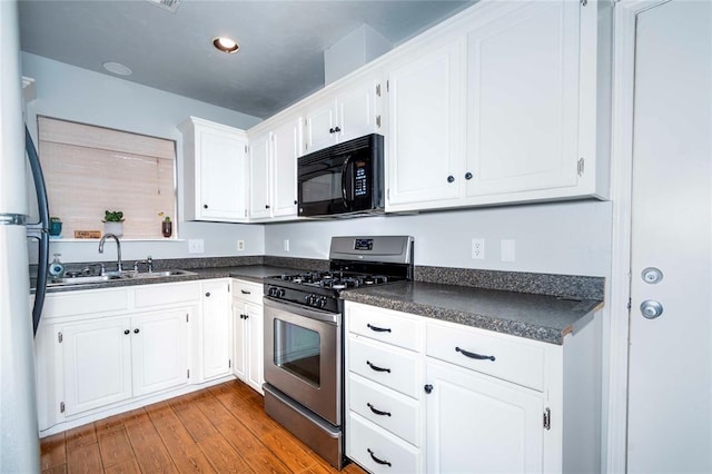 kitchen with wood finished floors, a sink, white cabinetry, appliances with stainless steel finishes, and dark countertops