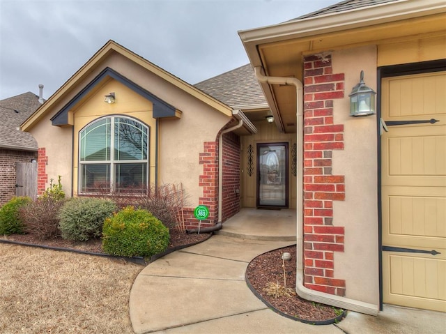 property entrance featuring stucco siding, a shingled roof, and brick siding