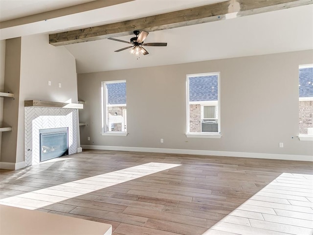 unfurnished living room with lofted ceiling with beams, a tile fireplace, wood finished floors, a ceiling fan, and baseboards