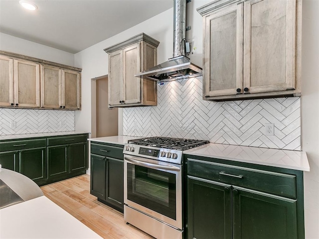 kitchen with tasteful backsplash, light wood-type flooring, wall chimney range hood, stainless steel range with gas cooktop, and green cabinets