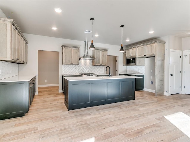 kitchen with light wood-style flooring, visible vents, stainless steel microwave, and wall chimney range hood