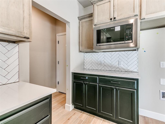 kitchen with light wood-type flooring, tasteful backsplash, stainless steel microwave, and light countertops