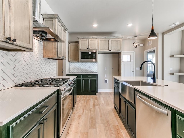 kitchen with tasteful backsplash, appliances with stainless steel finishes, light countertops, light wood-style floors, and a sink