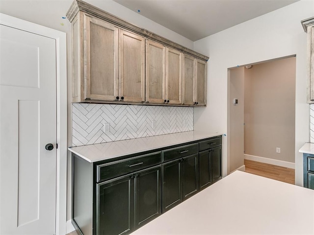 kitchen featuring baseboards, light countertops, light wood finished floors, and decorative backsplash