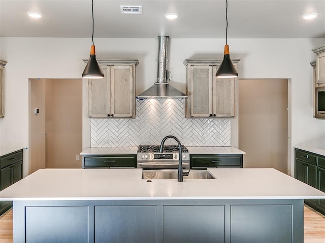 kitchen with tasteful backsplash, light countertops, visible vents, a sink, and wall chimney range hood