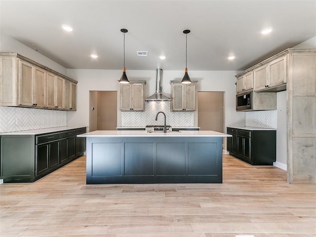 kitchen with light wood finished floors, visible vents, wall chimney exhaust hood, stainless steel microwave, and a sink