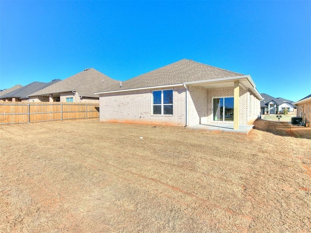 rear view of property featuring a shingled roof, brick siding, and fence