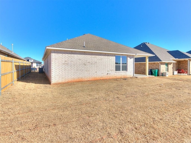 back of property featuring a yard, a shingled roof, fence, and brick siding