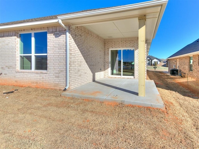 exterior space with cooling unit, brick siding, and a patio