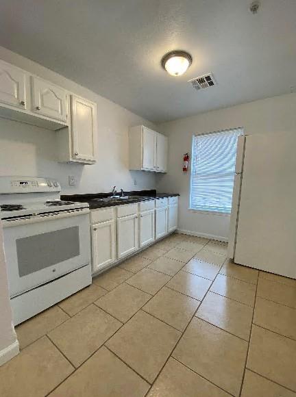 944 SE 14th St, Oklahoma City, OK 73129 - kitchen featuring dark countertops, visible vents, white cabinets, a sink, and white appliances