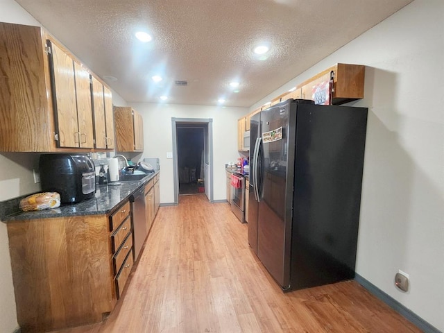 kitchen with a textured ceiling, stainless steel appliances, dark countertops, and light wood-style floors