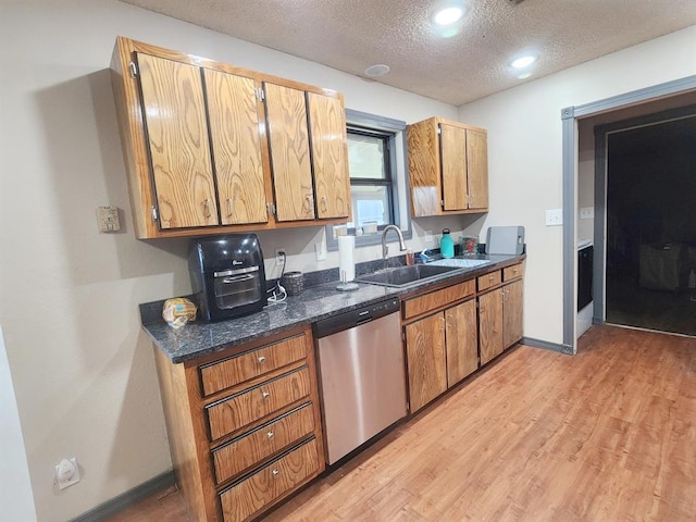 kitchen with light wood finished floors, baseboards, a textured ceiling, stainless steel dishwasher, and a sink