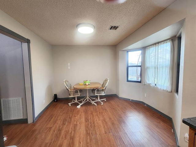 dining room featuring a textured ceiling, light wood-type flooring, visible vents, and baseboards