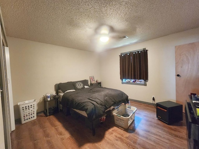 bedroom featuring baseboards, a textured ceiling, visible vents, and wood finished floors