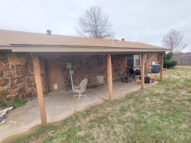 back of house with stone siding, a patio area, and a yard