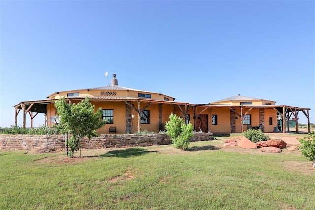 rear view of property featuring a chimney, a lawn, and stucco siding