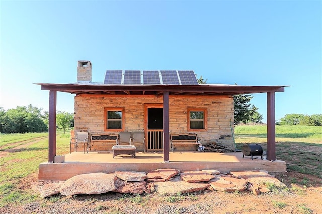 back of property with solar panels, a chimney, and a patio