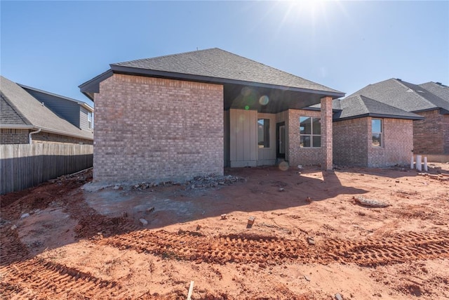 back of house featuring brick siding, roof with shingles, and fence