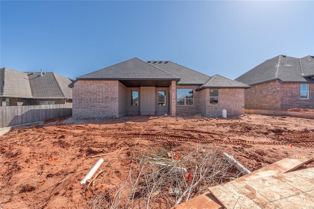 back of house with brick siding, roof with shingles, and fence