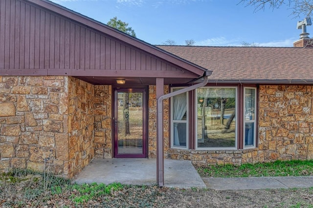 entrance to property featuring stone siding, roof with shingles, and a chimney